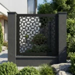 Czarny metalowy panel ogrodzeniowy z geometrycznym ażurowym wzorem zamontowany między ciemnymi słupkami przy nowoczesnym domu.