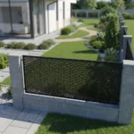 Metalowy panel ogrodzeniowy w czarnym kolorze z drobnym orientalnym ażurowym wzorem zamontowany między jasnymi słupkami przy nowoczesnym ogrodzie.