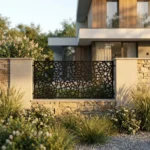 Metalowy panel ogrodzeniowy w czarnym kolorze z nieregularnym ażurowym wzorem przypominającym rozbite szkło zamontowany między jasnymi słupkami przy nowoczesnej posesji.