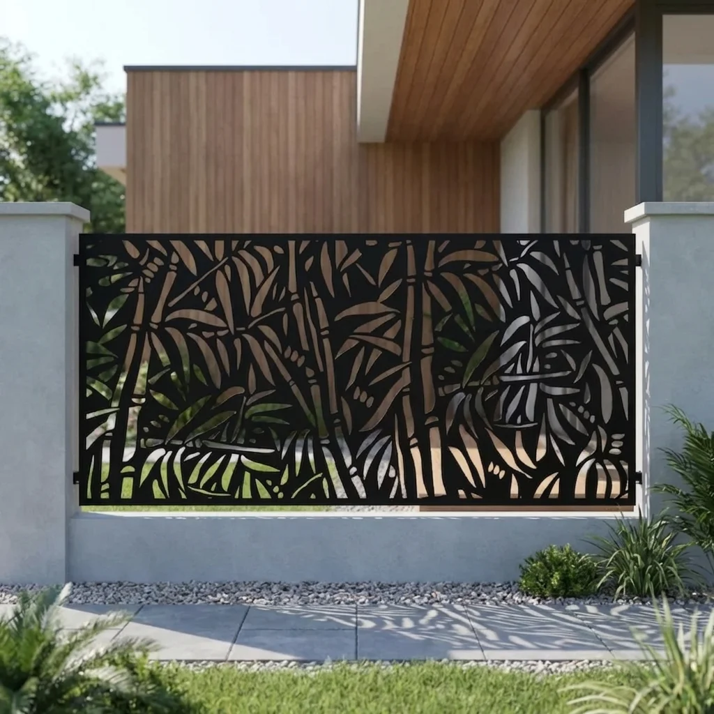 Metalowy panel ogrodzeniowy w czarnym kolorze z ażurowym wzorem bambusa i tropikalnych liści zamontowany między jasnymi słupkami przy nowoczesnym domu.