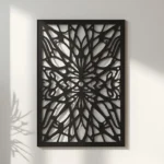 Czarny panel dekoracyjny z metalu o symetrycznym, geometryczno-roślinnym wzorze, zawieszony na jasnej ścianie.