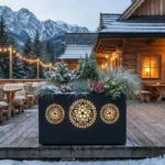 Czarna donica z podświetlanymi góralskimi rozetami na drewnianym tarasie przy górskim domu w zimowej scenerii