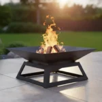 Nowoczesne metalowe palenisko tarasowe Steel Flame w kolorze czarnym, stojące na płytkach tarasowych z rozpalonym ogniem w środku.