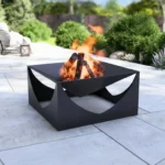 Czarne metalowe palenisko tarasowe Modern Arc o nowoczesnym, geometrycznym kształcie z półokrągłymi wycięciami, stojące na kamiennym tarasie z płonącym ogniem.