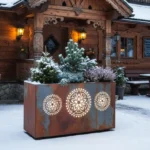 Metalowa donica LED z góralskim wzorem i podświetlanym logo przed góralską chatą w zimowej scenerii.