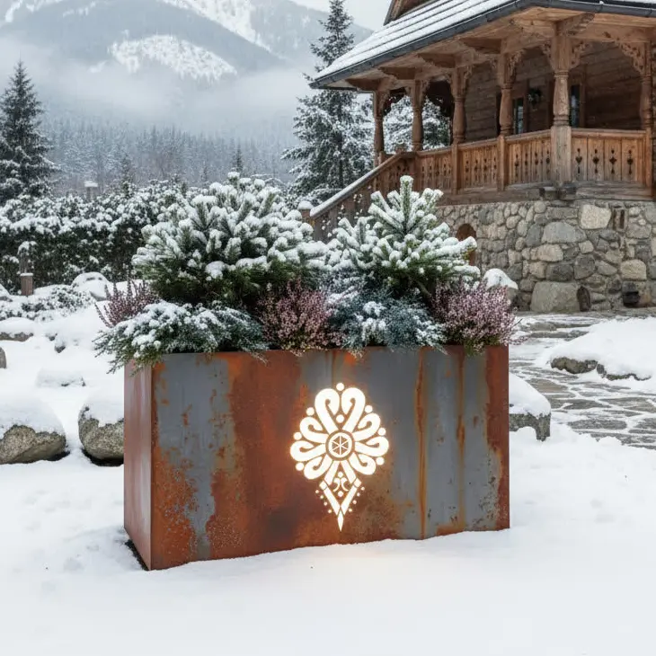 Metalowa donica LED z góralskim wzorem i podświetlanym logo przed góralską chatą w zimowej scenerii.