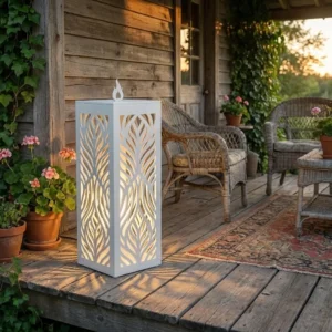 Metalowy lampion ogrodowy Cień Natury w kolorze białym z ażurowym roślinnym wzorem ustawiony na drewnianym tarasie w ogrodzie