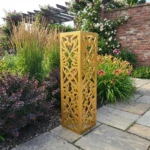 Kolumna ogrodowa metalowa „Serce Ogrodu” z symetrycznym, ażurowym wzorem ustawiona przy ścieżce ogrodowej