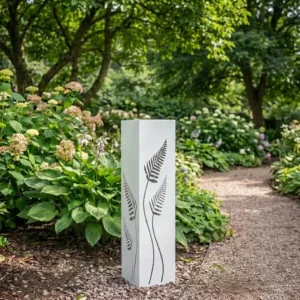 Biała kolumna ogrodowa metalowa „Ogród Paproci” z wyciętym motywem paproci ustawiona przy ścieżce w zielonym ogrodzie