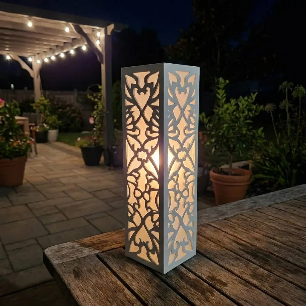 Metalowy lampion ogrodowy Serce Ogrodu z romantycznym ażurowym wzorem w nocnej aranżacji ogrodu