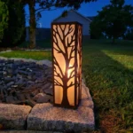 Metalowy lampion ogrodowy Drzewo Życia z ażurowym wzorem drzewa w nocnej aranżacji ogrodu