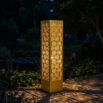 Metalowy lampion ogrodowy Złota Mozaika z ażurowym mozaikowym wzorem w nocnej aranżacji ogrodu