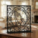 Dłonie Modlitwy w Ramie – metalowa dekoracja wolnostojąca ustawiona na drewnianej komodzie w eleganckim wnętrzu