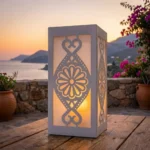 Lampion metalowy góralski Rozeta Podhalańska – biały lampion z motywem rozety ustawiony na drewnianym stole