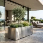 Metalowa donica prostokątna ze stali szczotkowanej do ogrodu z oliwką i trawami ozdobnymi na nowoczesnym tarasie